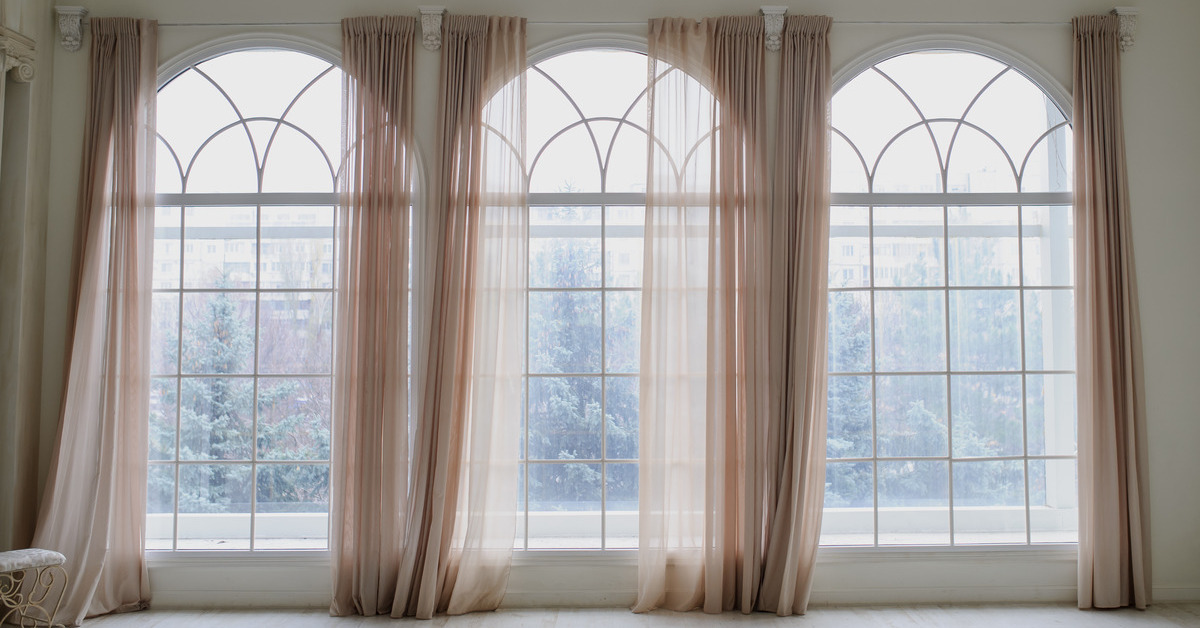 A large room with high ceilings and windows that take up most of the wall. Sheer pink curtains frame the windows.