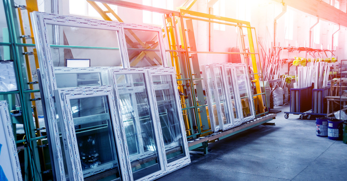 Light pours in from the windows of a warehouse with industrial materials and stacks of windows. There are both PVC and aluminum windows in the warehouse.