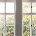 Two closed windows in a room with gray walls. The curtains are open and trees are visible through the windows.