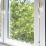 A closed window with white trim and handles. Green trees and portions of blue skies are visible through the glass.