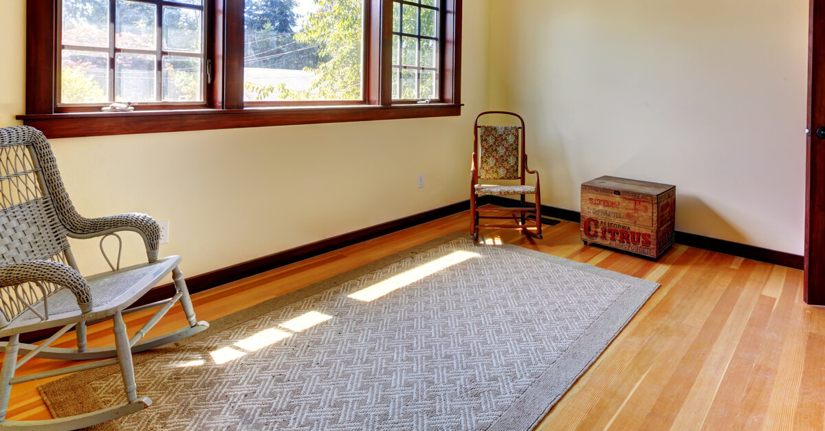 A room with hardwood floors, two chairs, large windows with wooden trimming, and a matching wooden door.